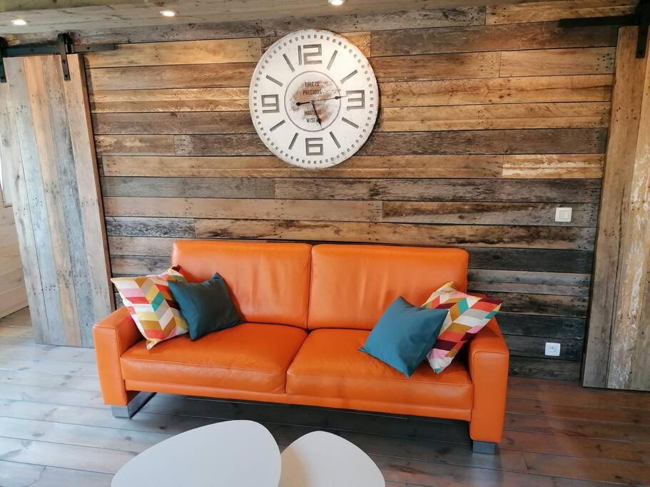 een oranje bank met kussens en een klok aan de muur bij Le canard: rustig genieten aan het water in Geel