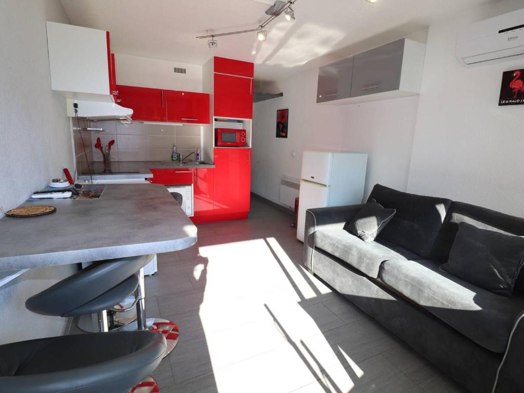 a living room with a couch and a kitchen with red cabinets at Studio Le Grau-du-Roi, 1 pièce, 4 personnes - FR-1-307-198 in Le Grau-du-Roi
