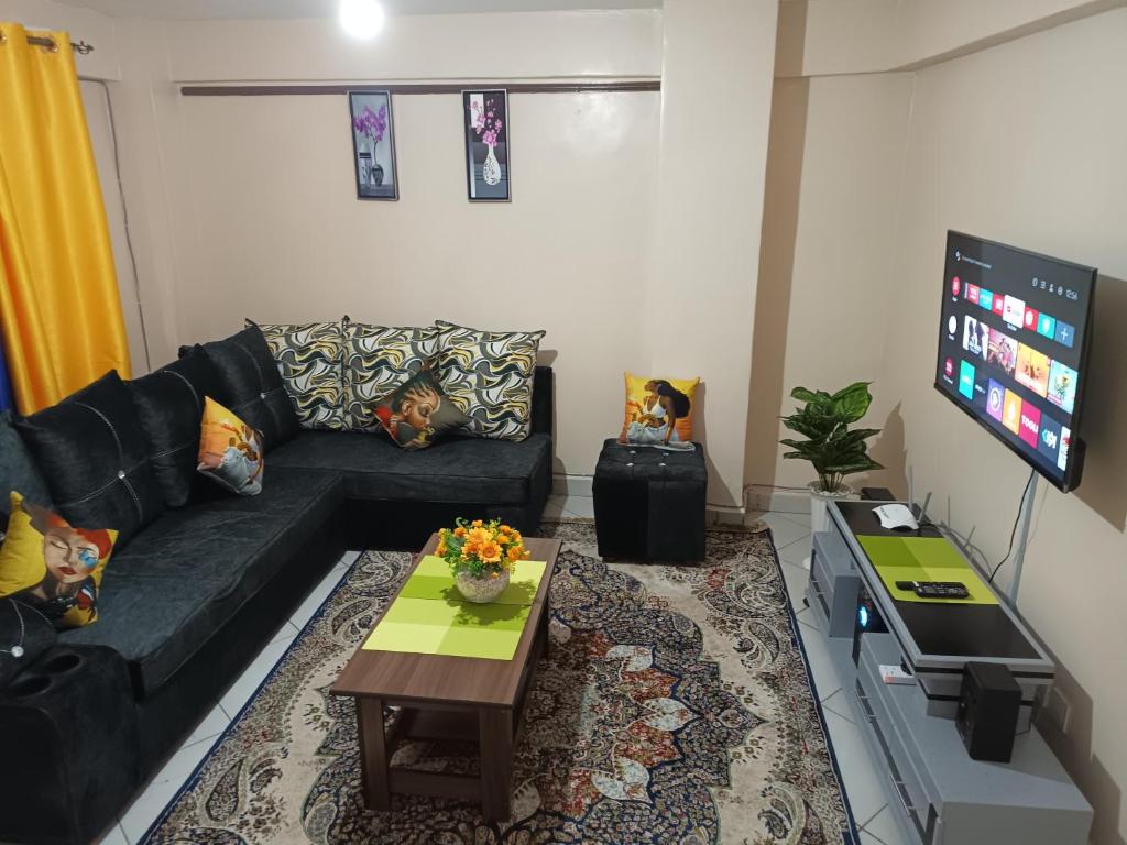 ein Wohnzimmer mit einem schwarzen Sofa und einem TV in der Unterkunft J.J homes 1- bedroom apartment, Nairobi in Nairobi