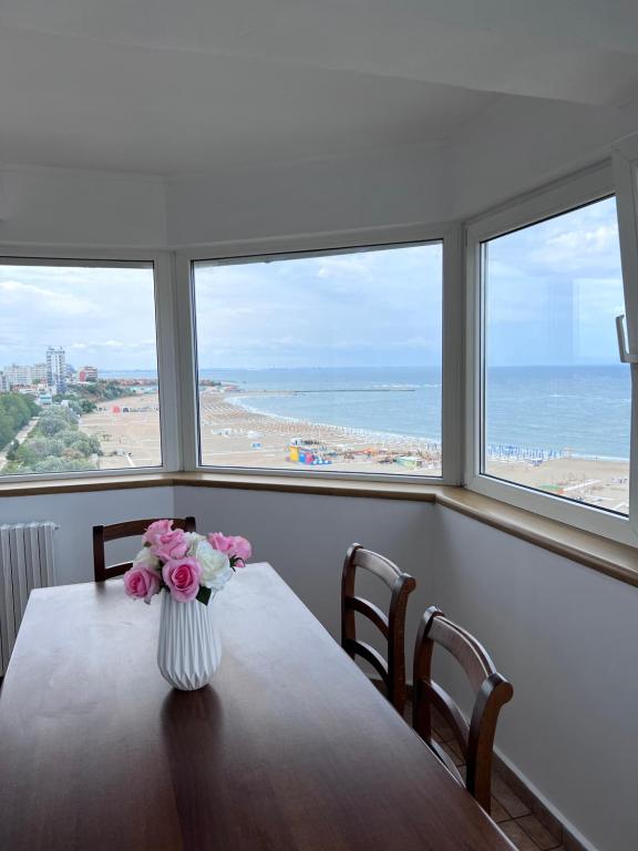 a vase of flowers on a table with a view of the beach at Panoramic Sea View Apartment in Constanţa