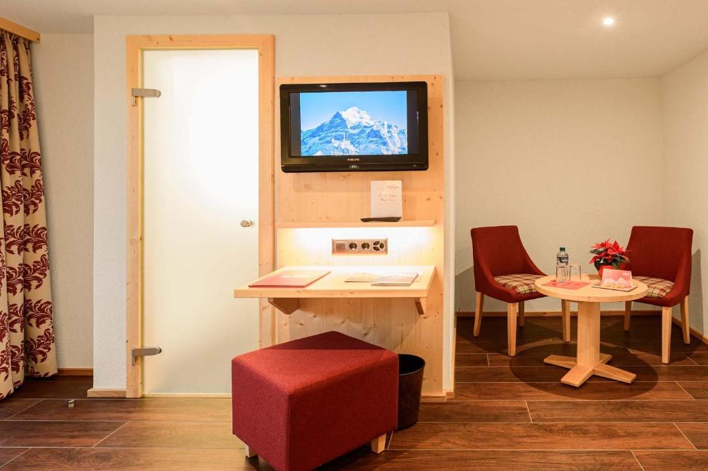 a room with a tv and a table and chairs at Hotel Caprice - Grindelwald in Grindelwald