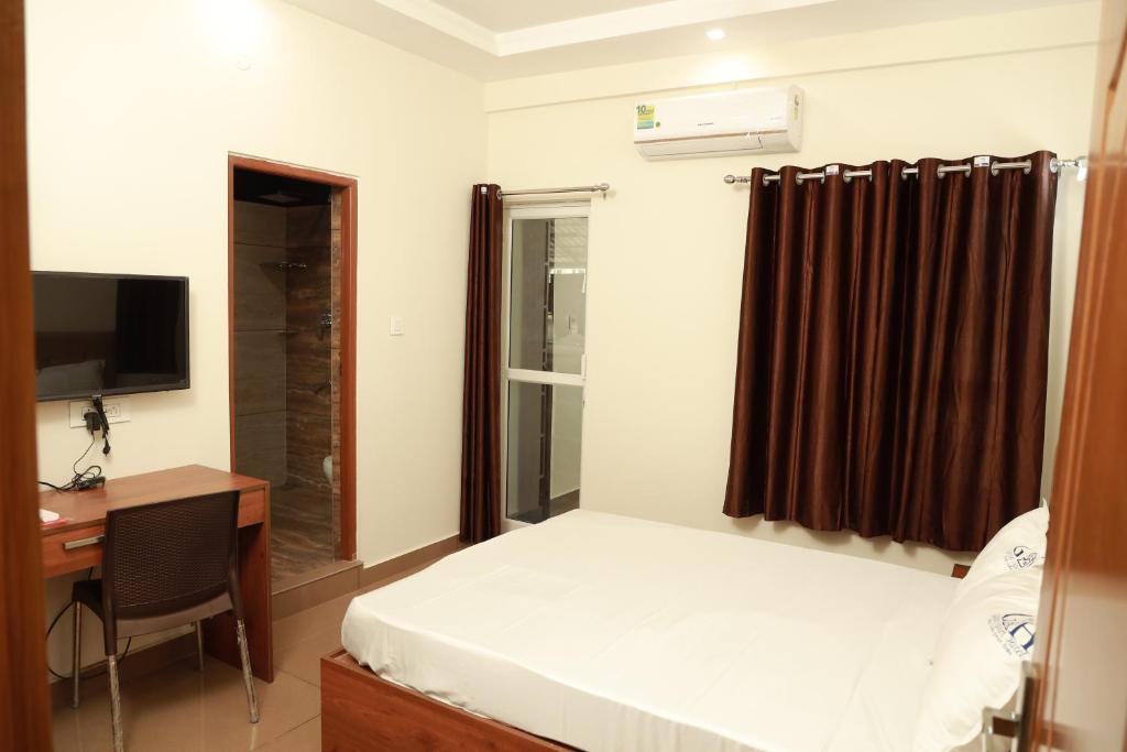 een slaapkamer met een bed, een bureau en een televisie bij Grace Apart Hotel @Kochi in Cochin