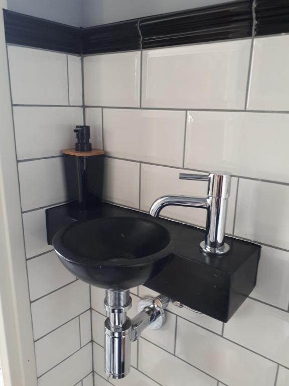 um lavatório preto numa casa de banho com azulejos brancos em De Malle Molen em Dinxperlo