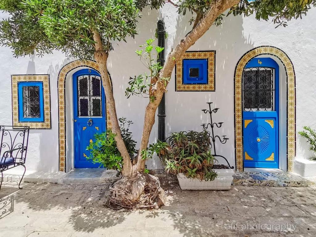 a tree in front of a building with blue doors at Hôtel Bou Fares in Sidi Bou Saïd