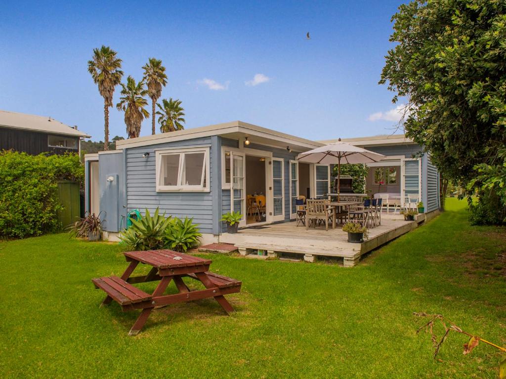 a blue house with a picnic table and an umbrella at Daisy Cottage - Hahei Bach in Hahei