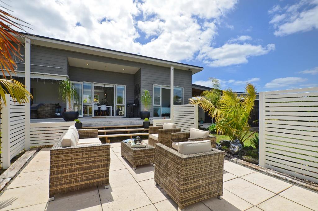 a patio with wicker furniture in front of a house at Little Pearl of Vista Verano - Mangawhai Home in Mangawhai