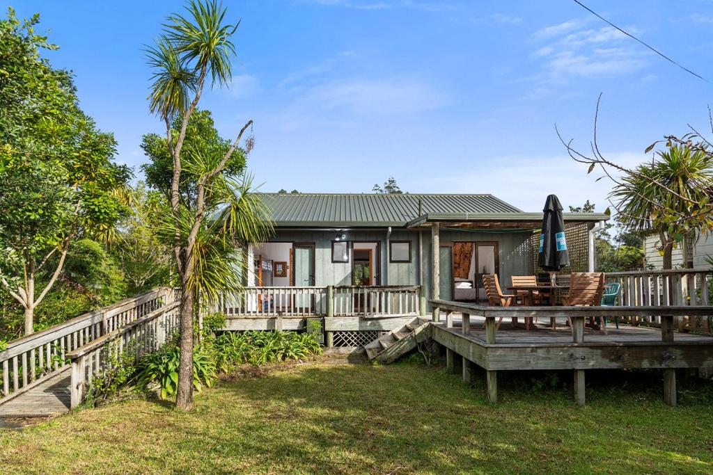 a house with a deck with a table and an umbrella at Riverview Retreat - Cooks Beach Holiday Home in Cooks Beach