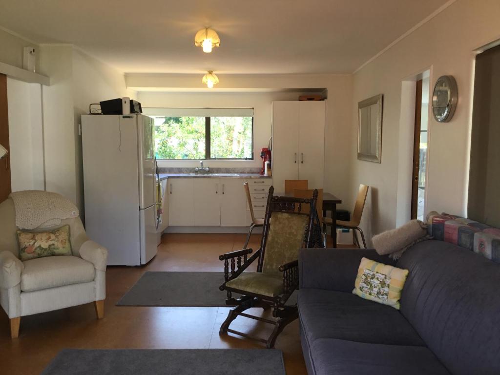 a living room with a couch and chairs and a kitchen at Ronas - Whiritoa Beach Bach in Whiritoa