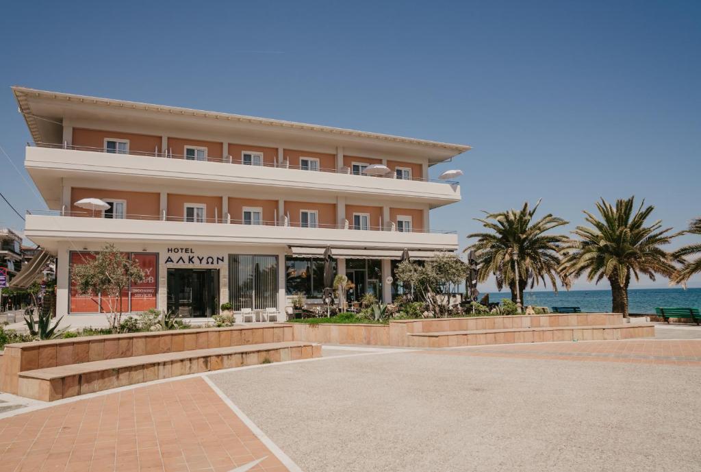 a large building with palm trees in front of the ocean at Hotel Alkyon in Paralia Katerinis
