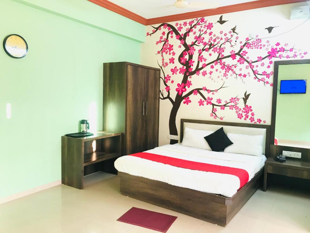 a bedroom with a bed with a tree painted on the wall at STAYMAKER Prakash International in Gonikoppal