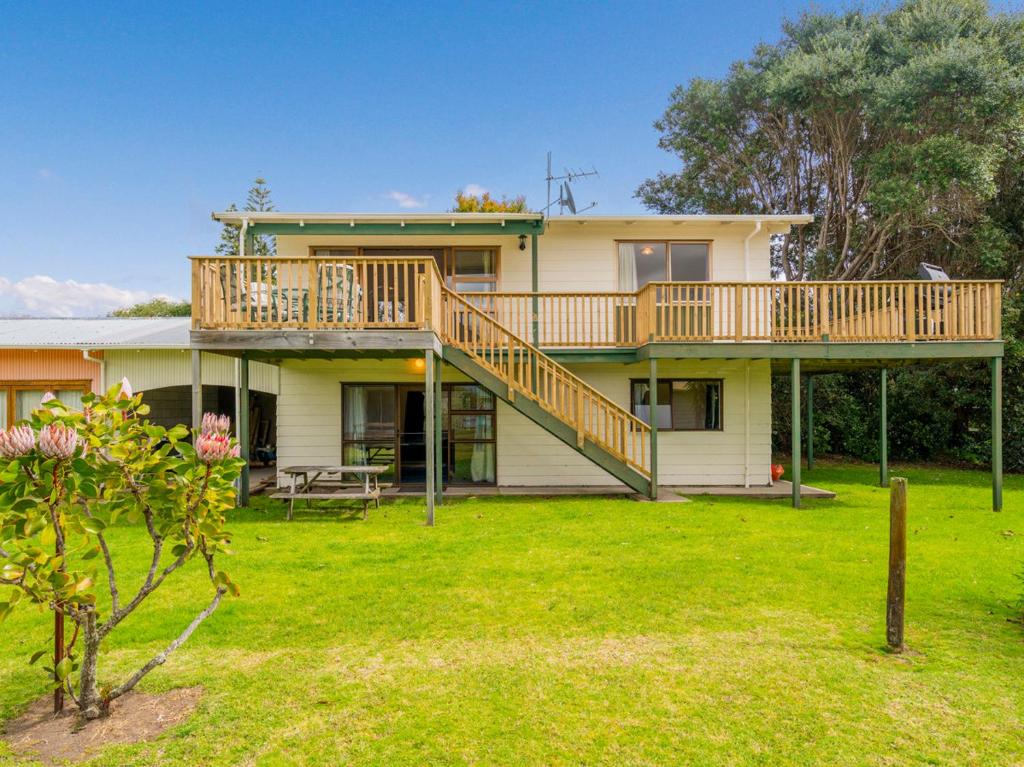 a large house with a deck on top of it at Oyster Bach - Cooks Beach Bach in Cooks Beach