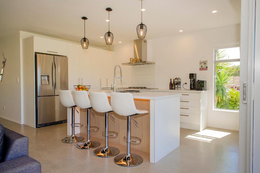 a kitchen with a bar with white stools in it at Paradise at Pauanui - Pauanui Holiday Home in Pauanui