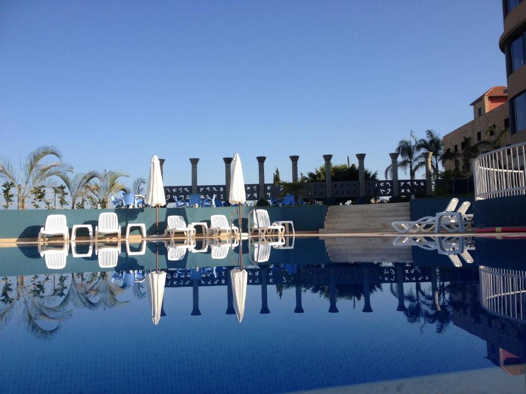 uma piscina de água com cadeiras e guarda-sóis em L'Hotel De Mon Pere em Jbeil