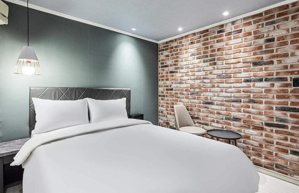 1 dormitorio con cama blanca y pared de ladrillo en Hotel WO Yongsan Station, en Seúl