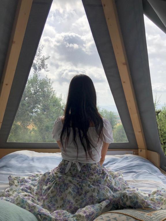 una niña sentada en una cama mirando por la ventana en Feudo Frammasi - Curte Glamping Experience, en Salve
