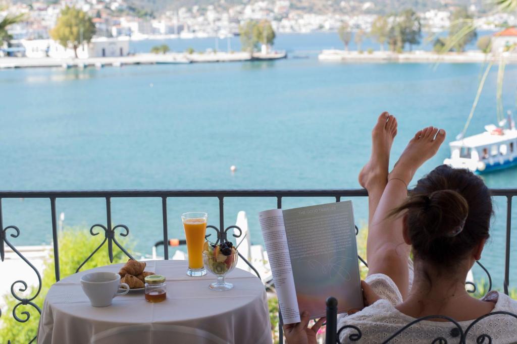 una mujer sentada en una silla leyendo un libro sobre una mesa en Theano Hotel en Poros