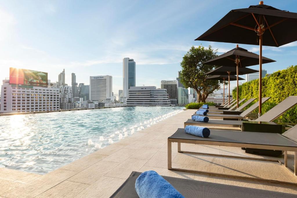 Ascott Embassy Sathorn Bangkok في بانكوك: مسبح عليه كراسي ومظلات فوق المبنى