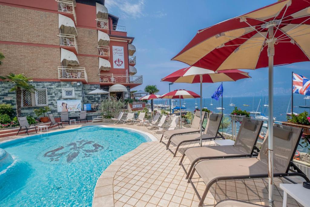 una piscina con sedie e ombrelloni accanto a un edificio di Hotel Firenze 3 Stelle Superior a Brenzone sul Garda