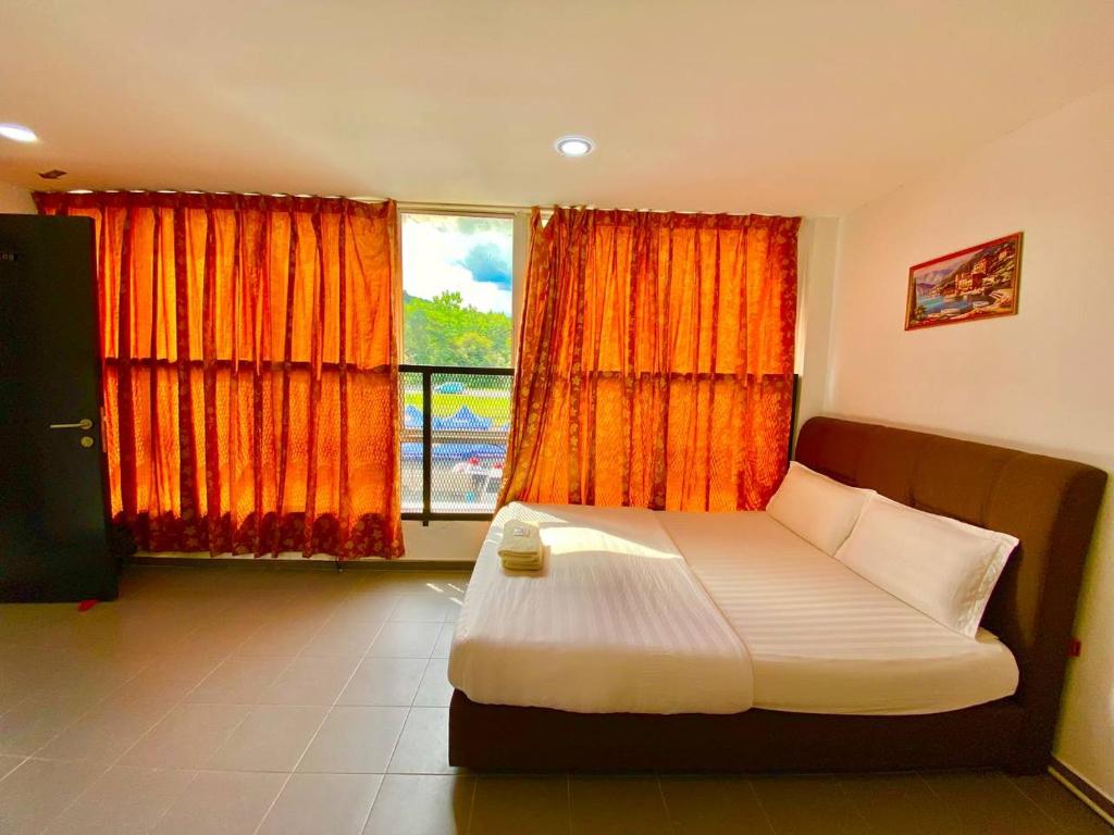 a bedroom with a bed with orange curtains and a window at LS VILLAGE HOTEL in Padang Besar