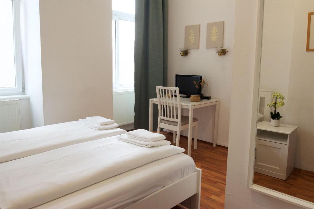 two beds in a room with a desk and a television at Hotel Pension ARPI in Vienna