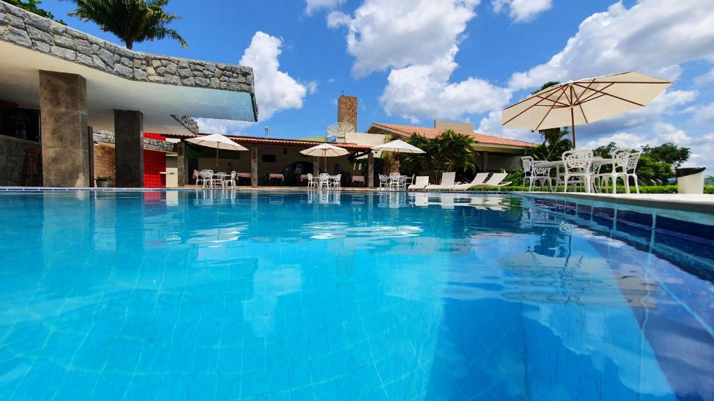 a large swimming pool with chairs and an umbrella at Hotel Três Palmeiras in Gravatá