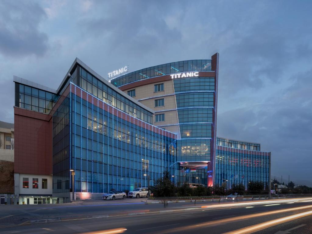 un gran edificio de cristal con coches estacionados frente a él en Titanic Hotel & SPA, en As Sulaymānīyah