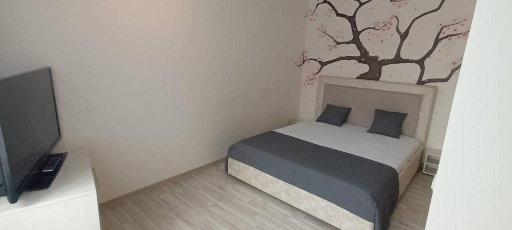 a bedroom with a bed and a tree on the wall at Old Town Apartments prie Vijūnėlės ežero in Druskininkai