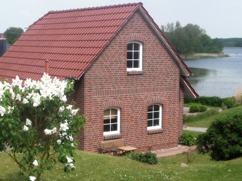 a red brick house with a bench in front of a lake at See in Sicht in Sternberg