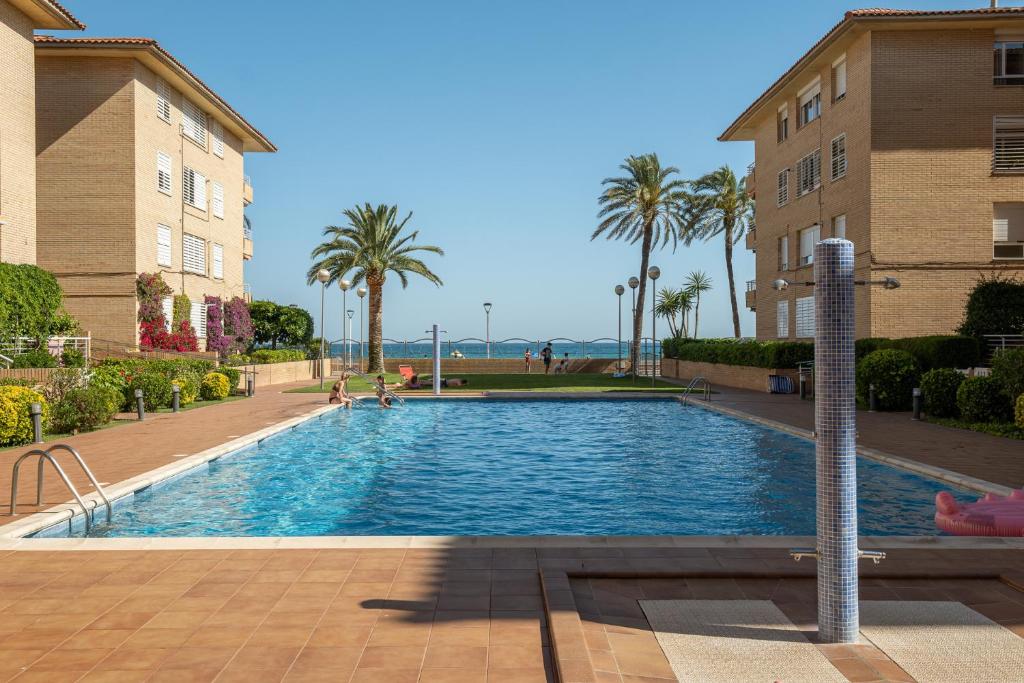 ein Pool mit Palmen und ein Gebäude in der Unterkunft Alma Home Vendrell Playa in Calafell