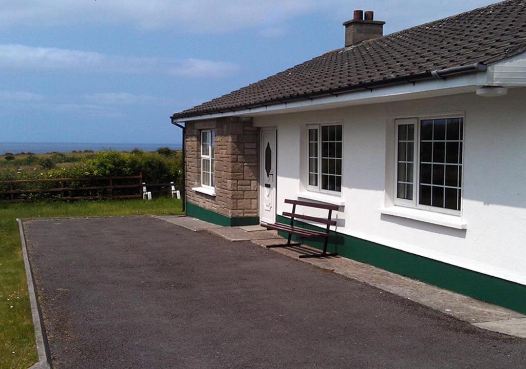 una casa blanca con un banco delante en Rossnowlagh Creek Holiday House, en Rossnowlagh