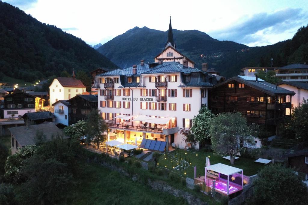 a large white building in a town with mountains at DU GLACIER Boutique & Traditions Hotel in Fiesch