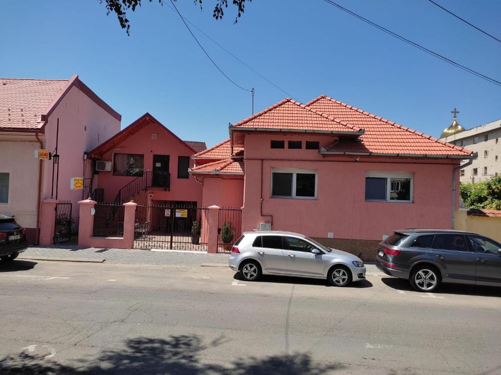 dwa samochody zaparkowane przed różowymi domami w obiekcie Calypso Rooms w Fogaraszu