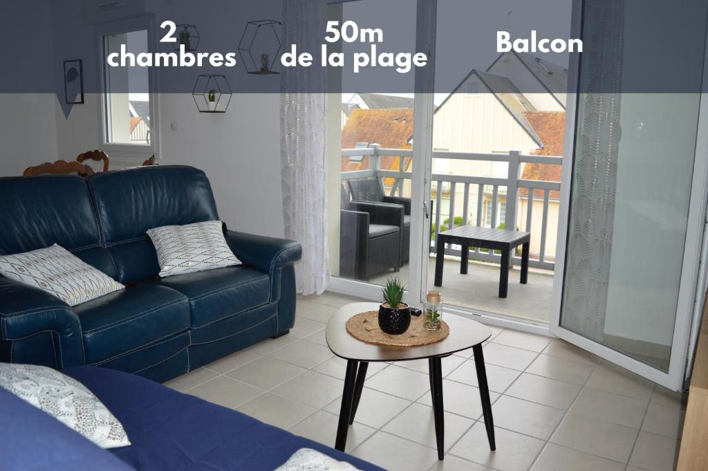 een woonkamer met een blauwe bank en een tafel bij Appartement spacieux avec balcon - à 50m de la plage in Courseulles-sur-Mer
