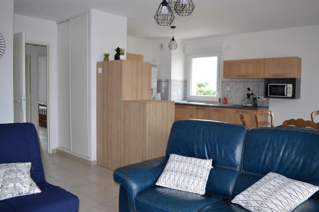 salon z niebieską kanapą i kuchnią w obiekcie Appartement spacieux avec balcon - à 50m de la plage w mieście Courseulles-sur-Mer
