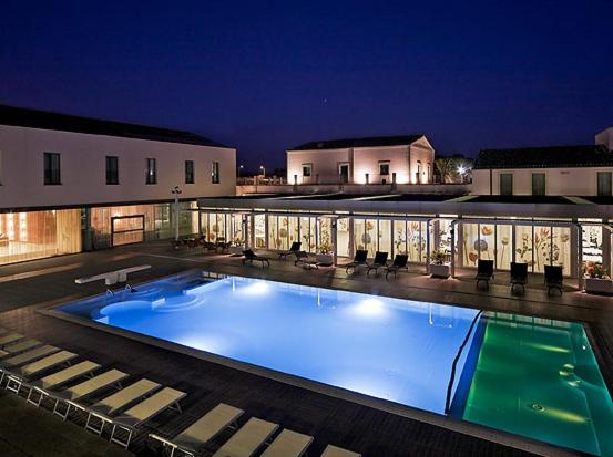 a large swimming pool in front of a building at night at Poggio Del Sole Hotel in Contrada Cimillà