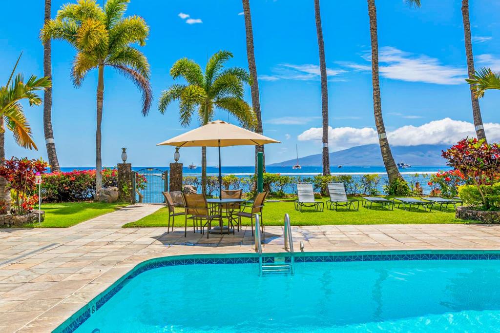 a pool with a table and chairs and palm trees at Lahaina Shores 202 in Lahaina