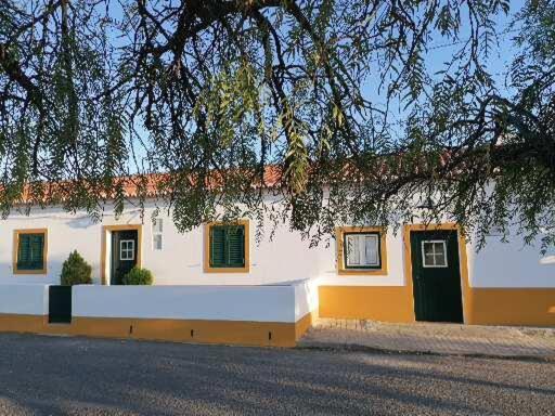 biały budynek z zielonymi oknami i drzewem w obiekcie A casa da Carolina II w mieście Mértola