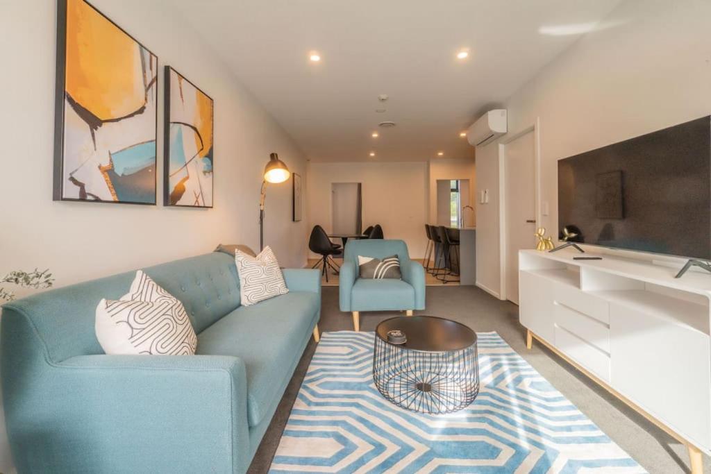 sala de estar con sofá azul y cocina en City Pulse Apartment with car park and city views en Auckland