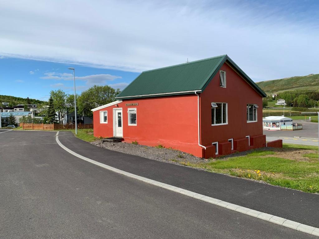 a red building with a green roof next to a road at Hofdi Guesthouse in Húsavík