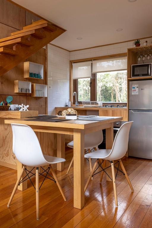 a kitchen with a wooden table and white chairs at Cabañas Arrayanes de Huillinco en Chiloé in Chonchi