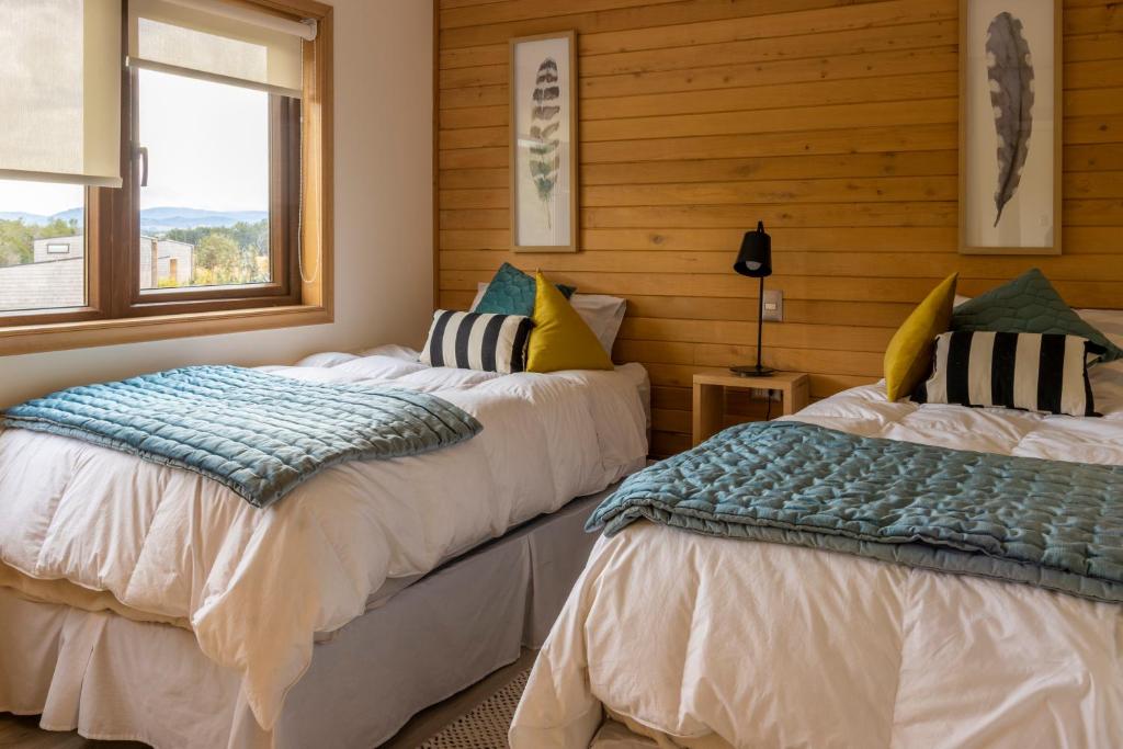 two beds in a room with wooden walls and a window at Cabañas Arrayanes de Huillinco en Chiloé in Chonchi