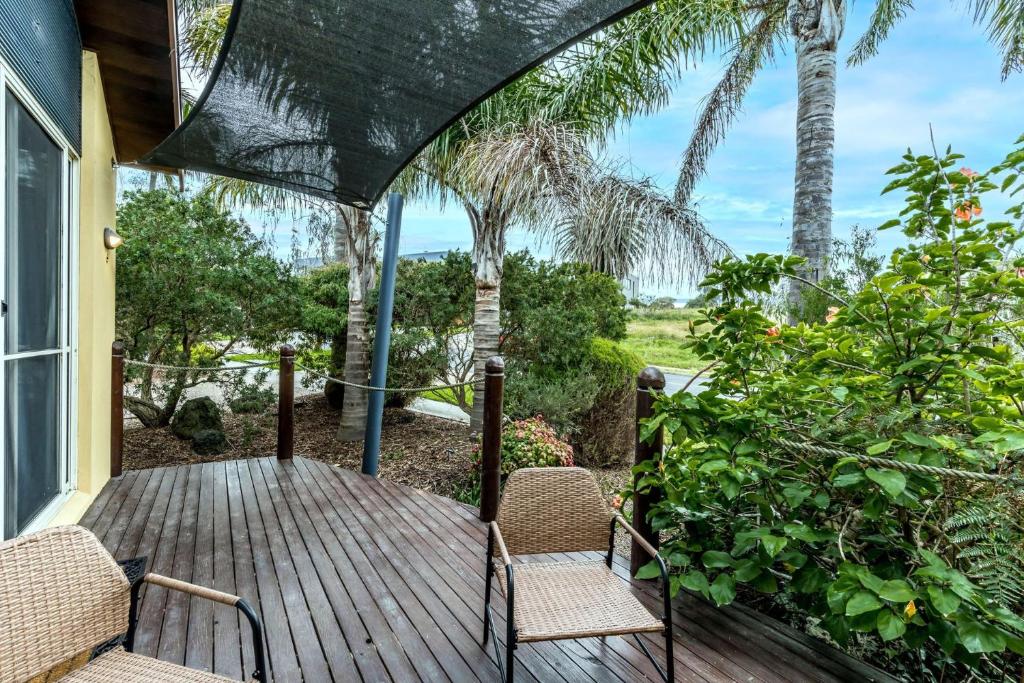 a wooden porch with two chairs and palm trees at Sails Five Inverloch in Inverloch