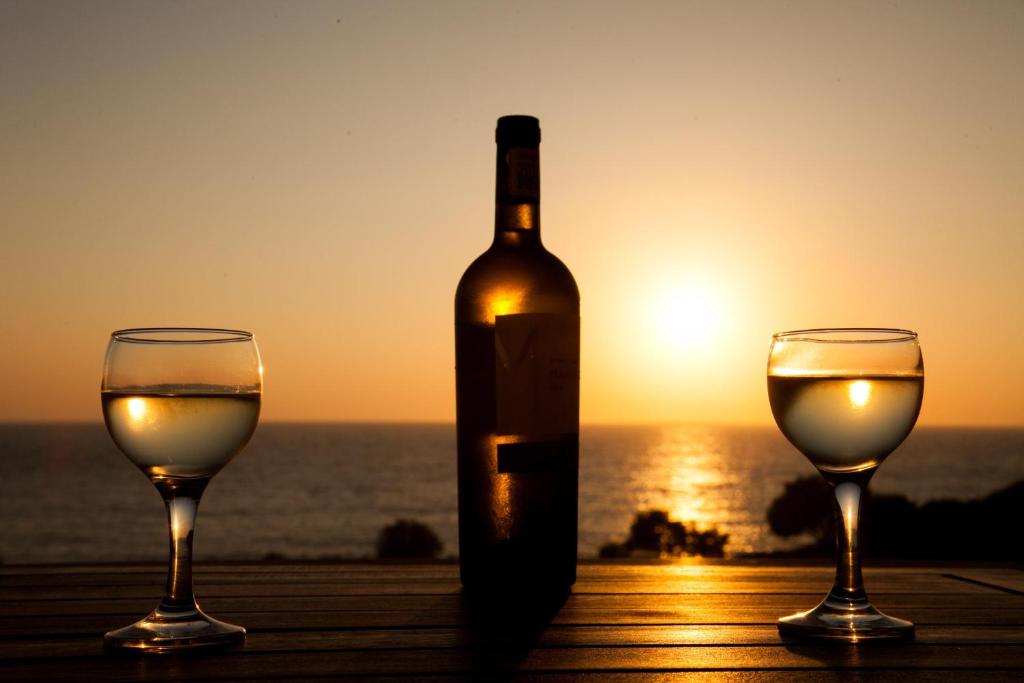a bottle of wine and two glasses on a table with the sunset at Mistral-Patmos in Patmos
