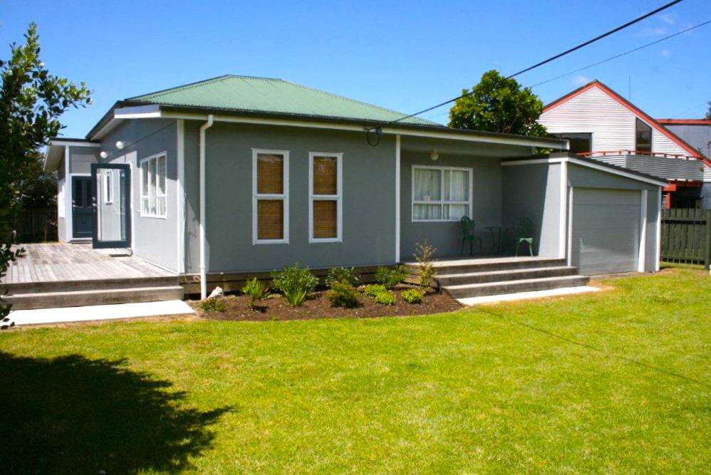 une petite maison avec une pelouse devant elle dans l'établissement Matapouri Cottage - Matapouri Holiday Home, à Matapouri