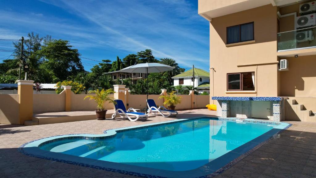 a swimming pool in front of a house with two chairs and an umbrella at Stone Self Catering Apartment in Grand'Anse Praslin