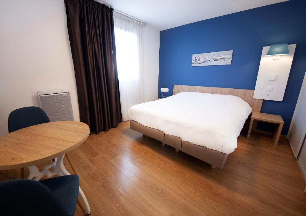 1 dormitorio con cama, mesa y pared azul en Residhome Clermont Ferrand Gergovia en Clermont-Ferrand