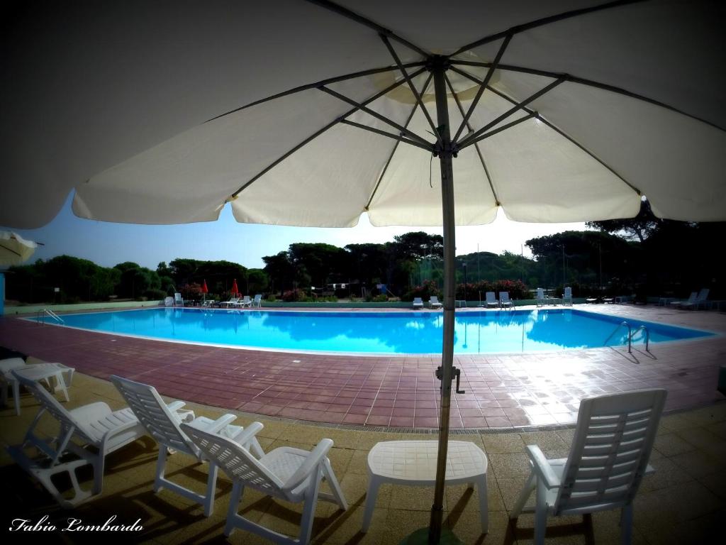 a table with an umbrella in front of a swimming pool at Camping Village S'Ena Arrubia in Arborea