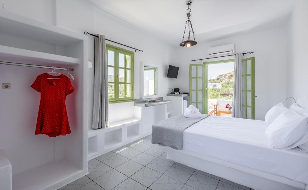 a white bedroom with a bed and a red dress on a rack at Pente Elies Milos in Pollonia
