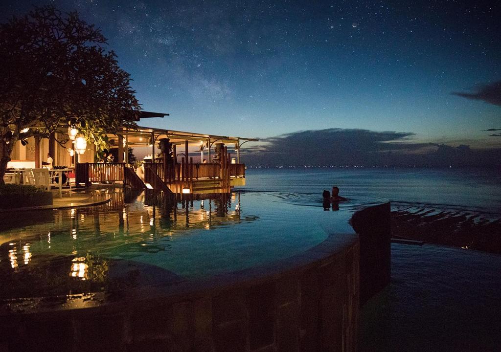 a child standing in a swimming pool at night at Anantara Uluwatu Bali Resort in Uluwatu