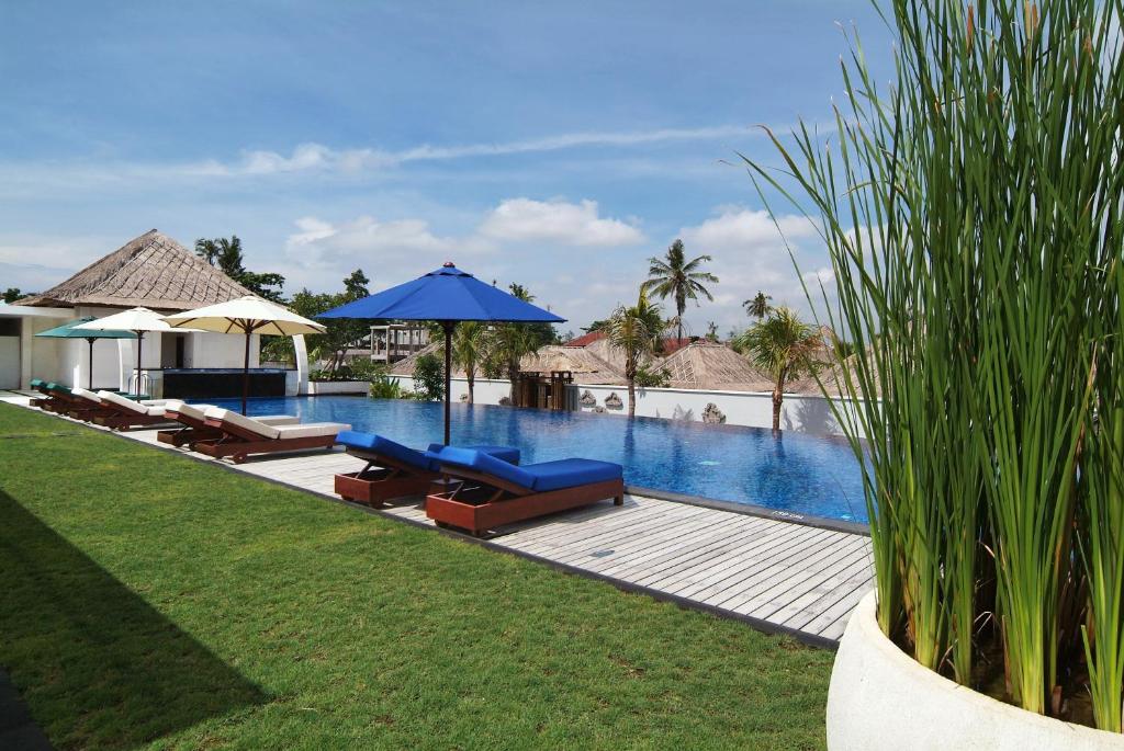 einen Pool mit Stühlen und Sonnenschirmen neben einem Resort in der Unterkunft Villa Mahapala in Sanur